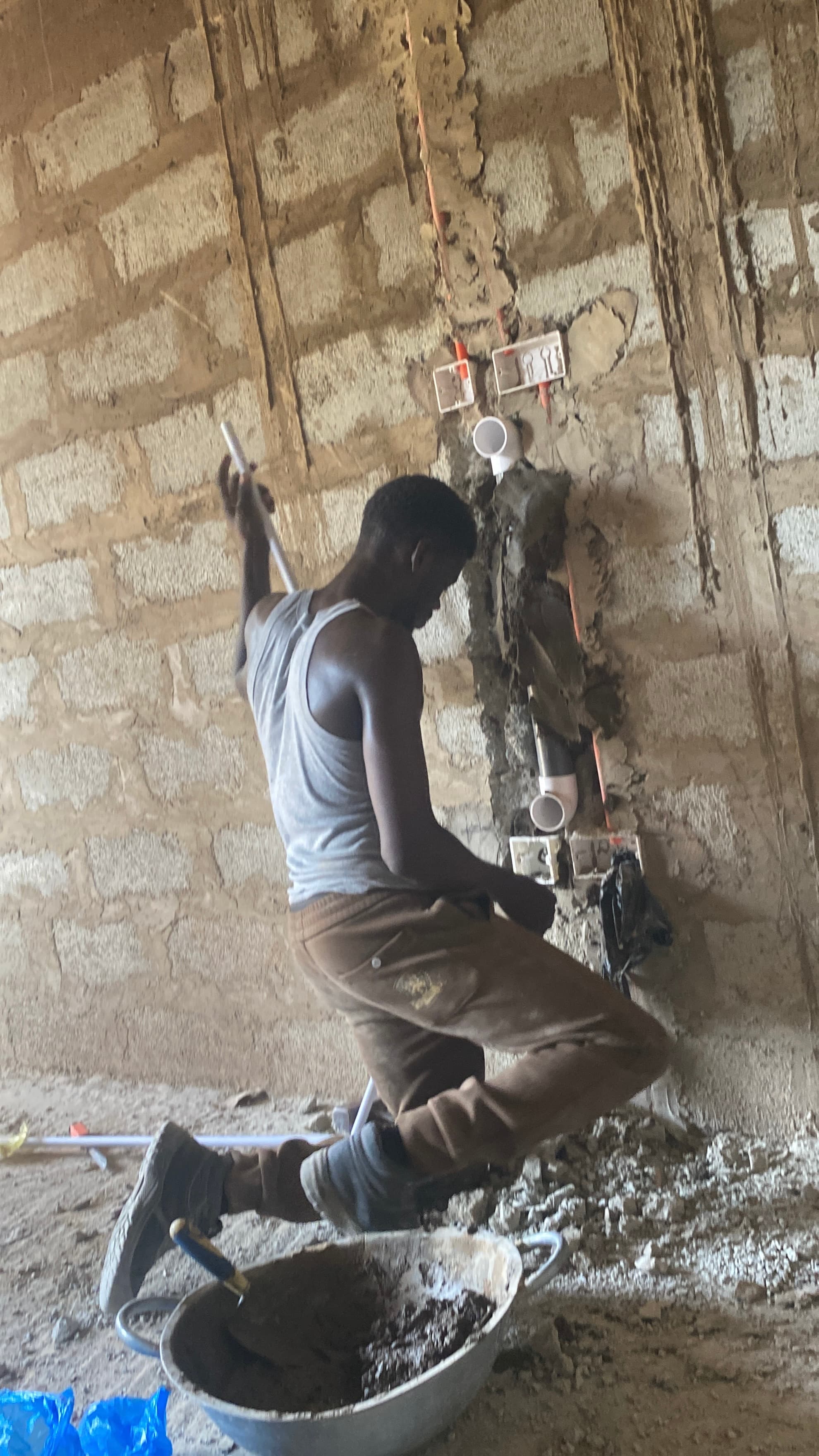 Electrician routing and terminating wall wiring behind sockets on a plastered wall