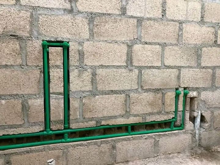 Green electrical conduit and plumbing pipes routed together along a block wall corner before plastering