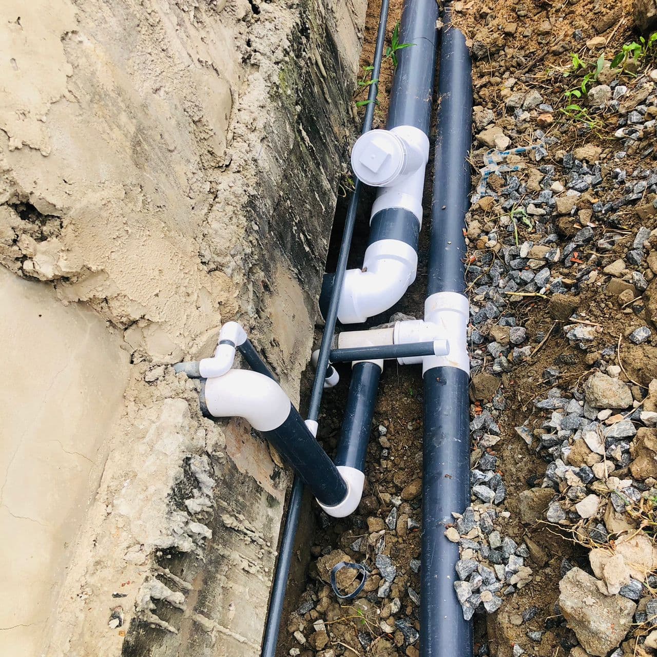 Underground PVC drainage and waste pipe fittings laid in a trench alongside a foundation wall